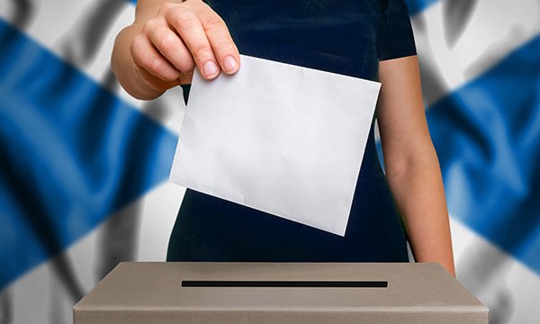 Picture shows a figure placing a vote in a ballot box, with the Scottish flag in the background