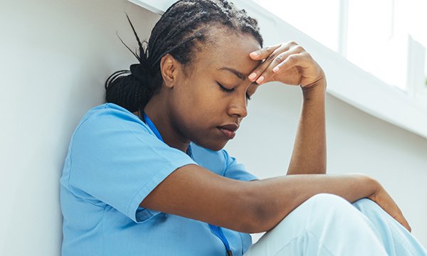 Picture of a nurse with her hand on her forehead looking depressed