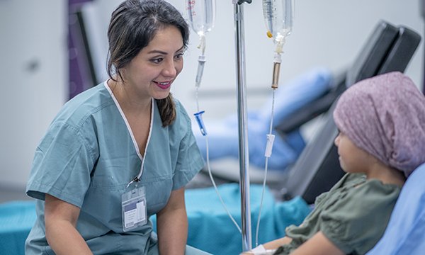 A nurse chatting at the bedside of a young child: standardised training would help nurses administer systemic anti-cancer therapy for children and young people across trusts