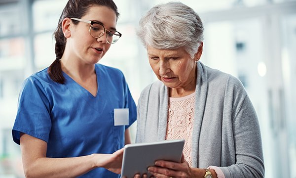 Nurse with older woman looking at a tablet computer detailing her patient record: dementia diagnosis rates could be improved by a diagnostic tool with five criteria to check 