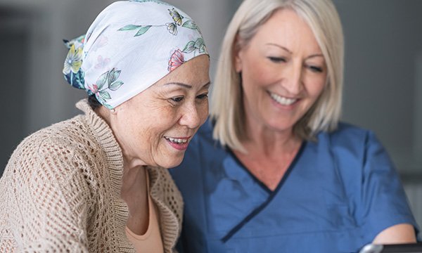 A woman wearing a bandana to hide her hair loss talks through her cancer treatment plan with a female healthcare professional