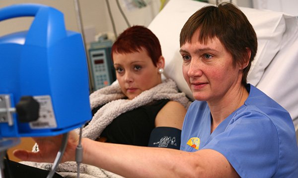 A nurse takes a reading from a monitor attached to a young woman in an oncology unit
