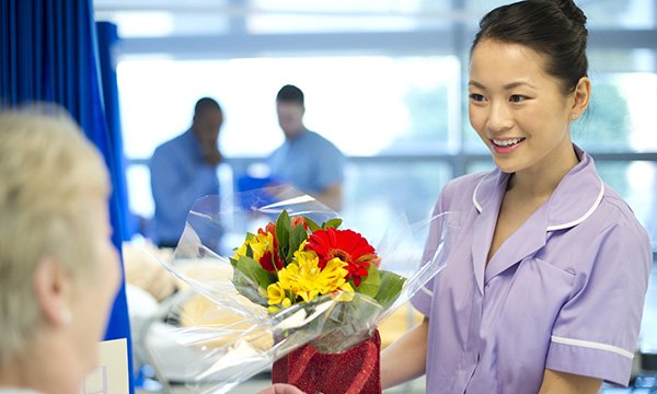 A smiling nurse receiving a bouquet of flowers from a patient