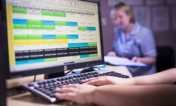 Close up of a hands on a keyboard in front of a computer screen showing a staff rota being planned