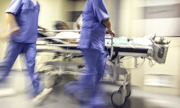 Nurses rushing along a hospital corridor push a wheeled stretcher on which a patient is lying