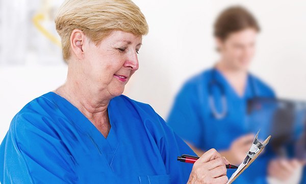 A happy looking older nurse writing notes on a clipboard