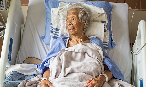 An older woman who is living with frailty lies in a hospital bed