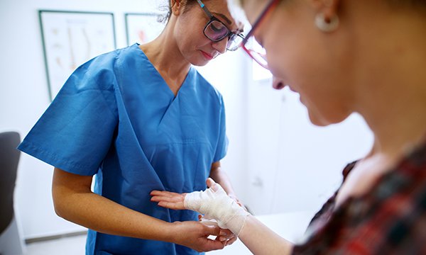 General practice nurse nurse bandages a patient's hand and wrist – many practice staff may be waiting for this year's pay rise