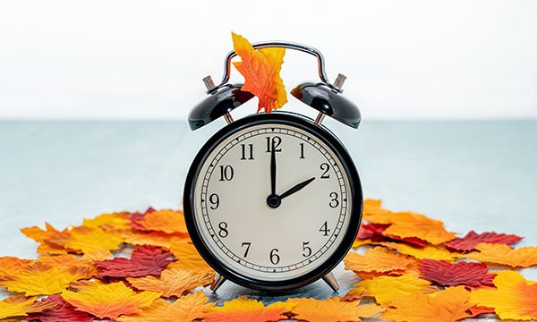 Photo of a clock surrounded by fallen leaves, illustrating a story about clocks going back in October
