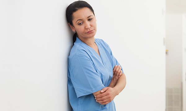 Nurse leans on wall looking dejected – as guidance aims to help NHS staff address workplace bullying