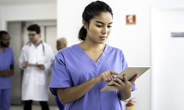 Nurse standing in a hospital room making notes on an electronic tablet