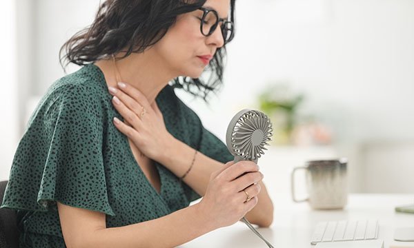 A woman holds a mini fan near her face as she experiences a hot flush, a common symptom of menopause
