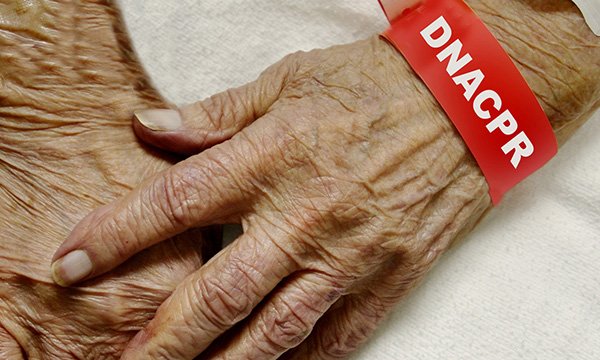 A close-up of an older person’s had with a red wristband saying DNACPR