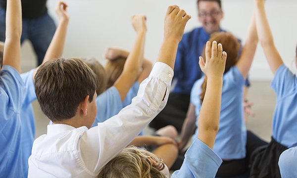 Children in a classroom putting their hands up 