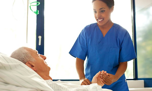 nurse holds patient's hand at bedside