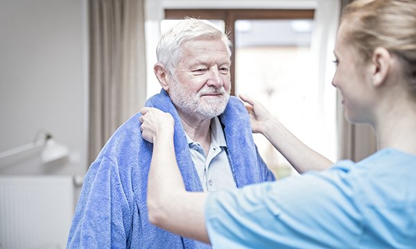 Carer helping man put on dressing gown