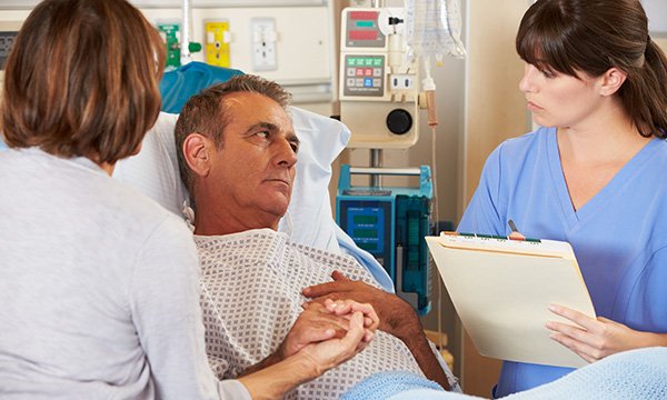 A man in a hospital bed having a conversation with a nurse who is attending him