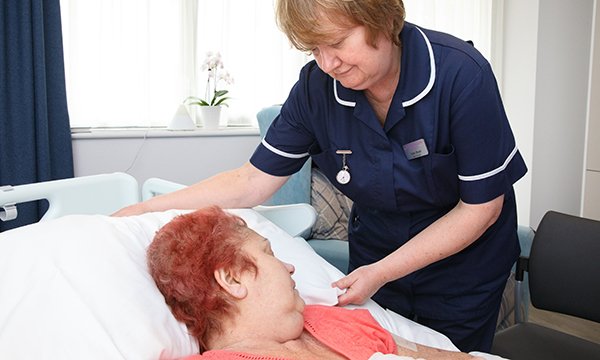 A nurse adjusting a patient's pillow in a hospital bed