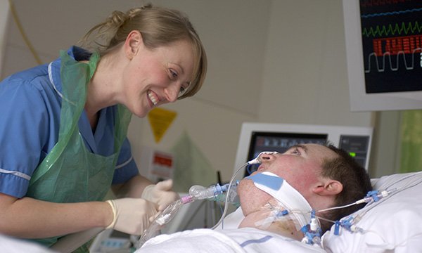 A staff nurse tends to a patient on a respirator in a hospital bed.