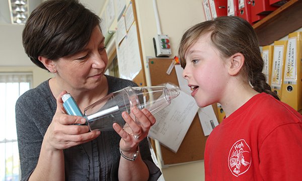 A teacher helps a pupil with an asthma spacer/inhaler