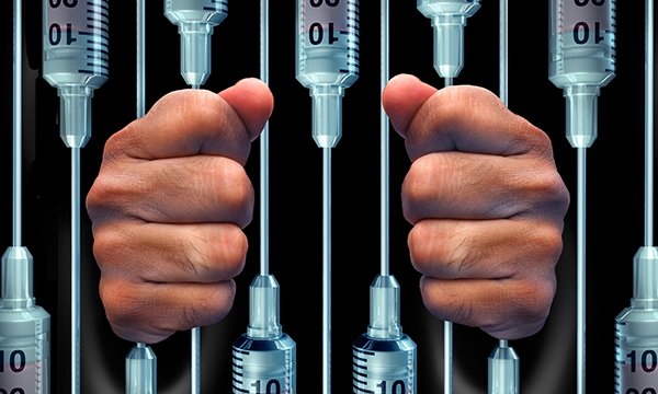 hands around syringes arranged like prison bars