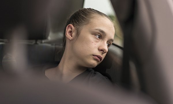A girl looking sad, staring out of a backseat car widow