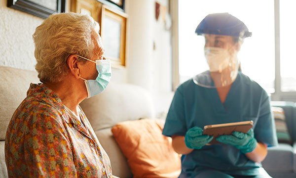 A nurse in PPE talking to an elder lady with a face mask. Approximately 27% of US COVID-19 deaths have been nursing home residents. Picture: iStock