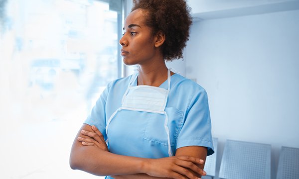 A woman in scrubs standing in a clinical area, reflecting on her experiences at work