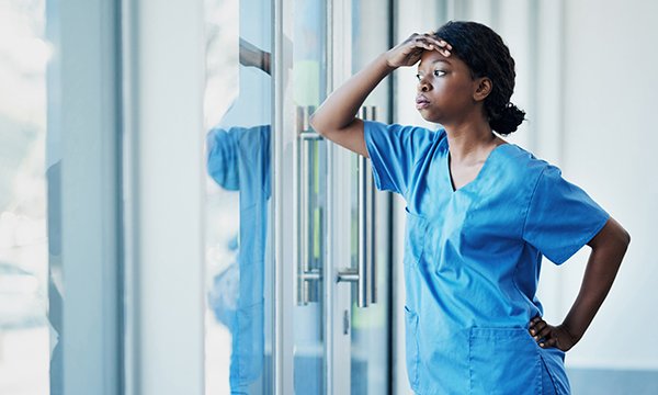 Nurse leans against a window, puffing out her cheeks and looking exhausted