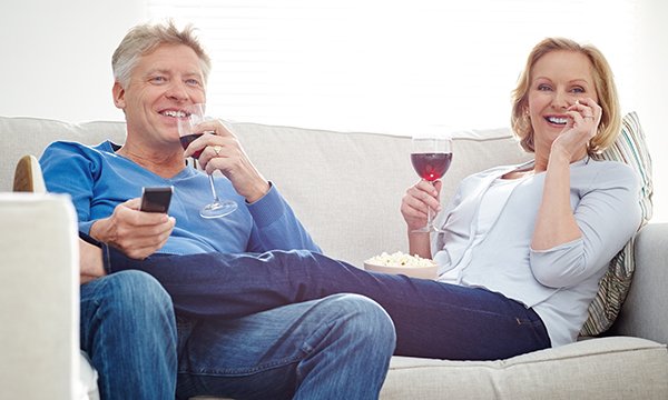 man and woman snuggle on sofa, smiling and drinking wine