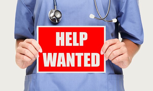 nurse's hands hold up sign saying 'help wanted'