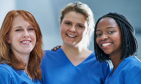 Three nurses stand together, smiling