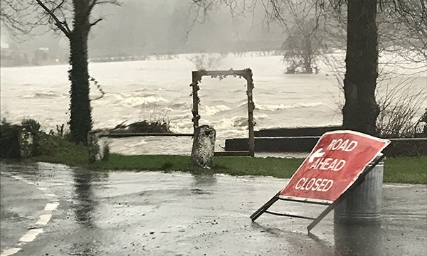 flooded country road, with battered 'road ahead closed' sign