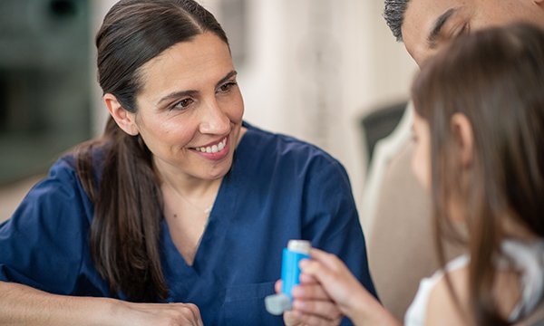 Picture of a medic showing a girl how to use an inhaler. Updated guidance from NICE emphasises importance of regular use rather than higher dose of inhaled corticosteroids in children and young people.