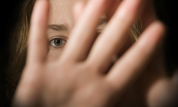 Picture shows a woman holding a hand in front of her face protectively.