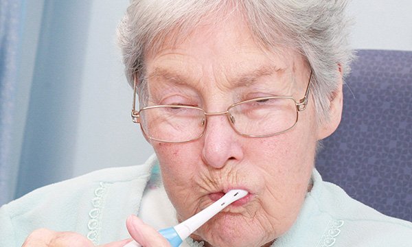 Picture shows an older woman holding a toothbrush in her mouth