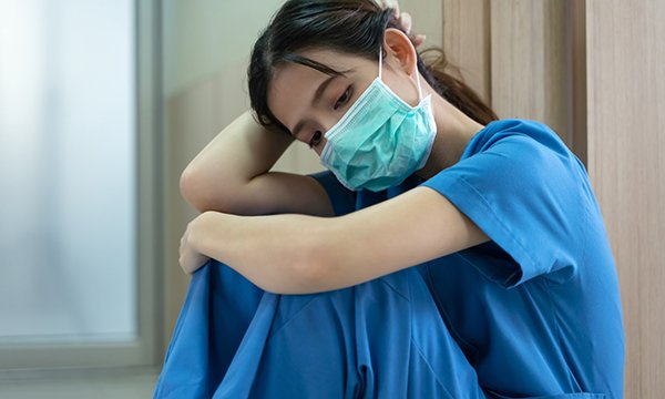 Nurse dressed in scrubs and face mask slumps and looks exhausted as nurse leaders employers to protect staff ahead of a second wave of covid-19