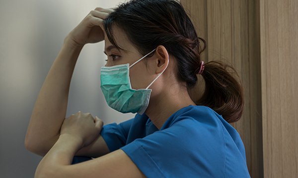 Nurse sits with head in hand, looking drained