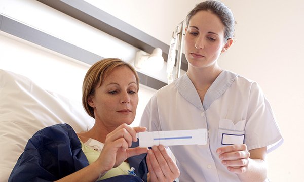 Nursing student stands at bedside assessing patient's pain using pain scale