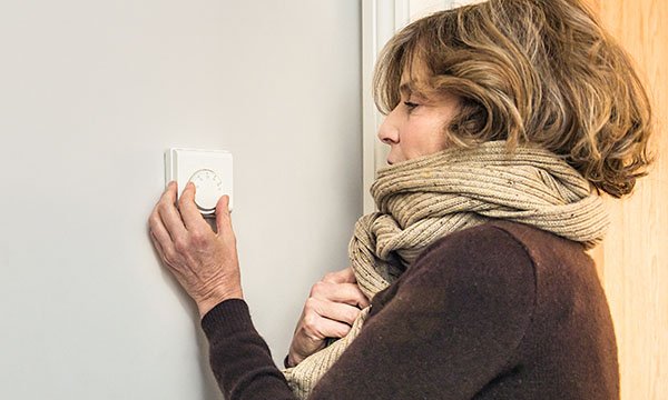 Woman wrapped up in heavy scarf adjusts her central heating control as energy price hikes loom