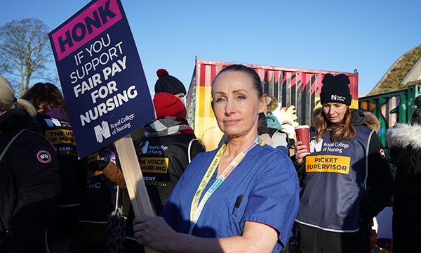 Nurse holds banner on RCN picket line, with fellow strikers in the background