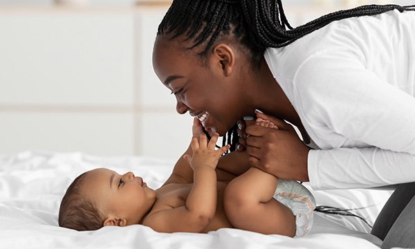 Smiling woman holds baby’s feet as she gazes at the infant – IFS research found female nurses in more male teams take less maternity leave, and career progression slows after motherhood
