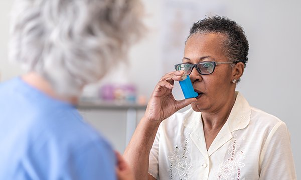 A senior black women with asthma learning how to use an inhaler with the help of a female healthcare professional: affecting more than 9 million people, asthma and COPD are the first and second most common lung diseases in the UK
