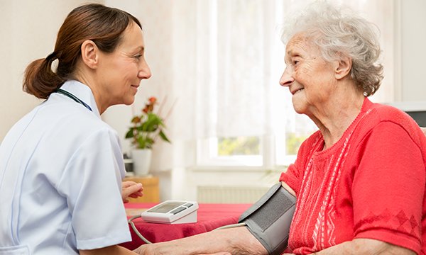 District nurse checking the blood pressure of an older female patient at her home