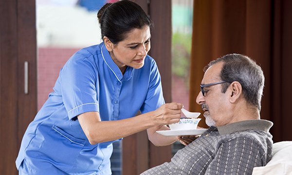 A nurse spoon feeds a seated man: social care leaders have welcomed a £600 million investment boost
