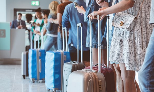 Long queue of travellers with suitcases at airport check-in, illustrating rise in numbers of nurses emigrating from Scotland