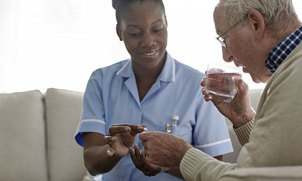 Nurse in a care home hands a man a tablet, which he takes with a glass of water