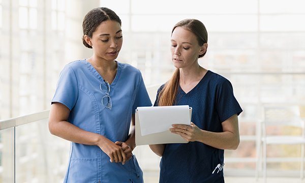 Two nurses discuss a file that one of them is holding