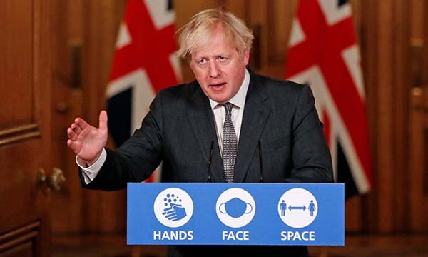 Former prime minister Boris Johnson standing at a podium with Hands Face Space written on it during the COVID-19 pandemic
