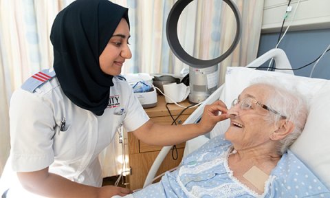A smiling nursing student at the bedside of an older patient: paid placements might encourage more people into the profession, say nurses 